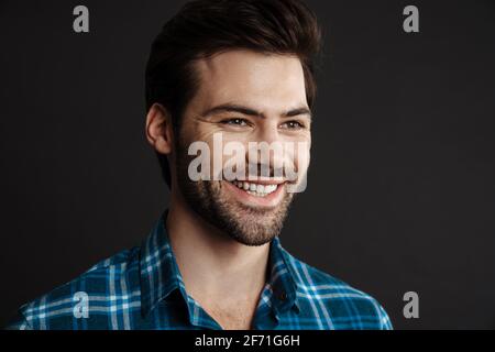 Joyful handsome brunette guy smiling and looking aside isolated over black background Stock Photo