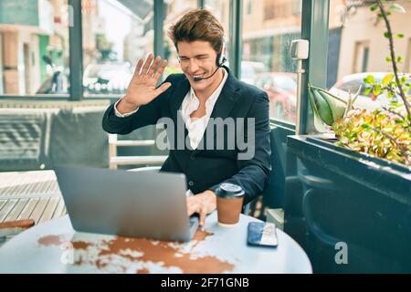 Young caucasian businessman with smiling happy doing video call using laptop at coffee shop terrace. Stock Photo
