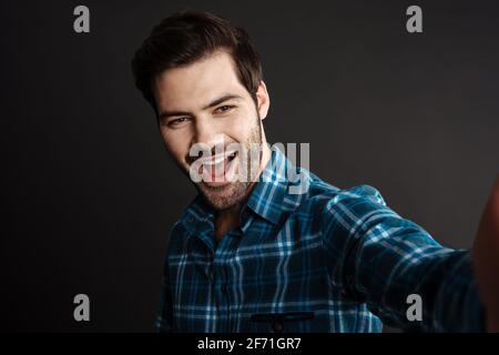 Joyful handsome unshaven guy smiling while taking selfie isolated over black background Stock Photo