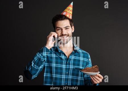 Smiling guy talking on cellphone while posing with birthday cake isolated over black background Stock Photo