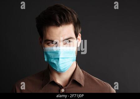 Pleased handsome young man posing in protective mask isolated over black background Stock Photo