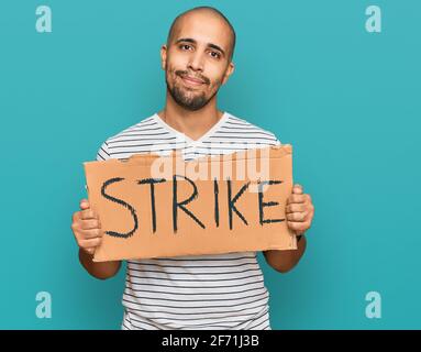 Hispanic adult man holding strike banner cardboard thinking attitude and sober expression looking self confident Stock Photo