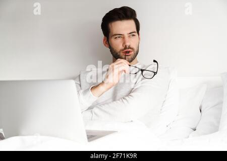 Focused handsome man using laptop while resting in bed at home Stock Photo