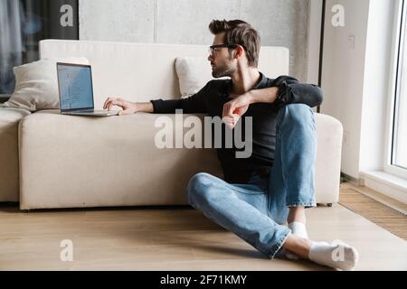 Focused unshaven man using laptop while sitting on floor at home Stock Photo