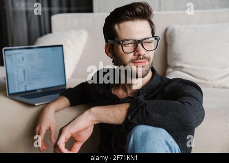 Pleased unshaven man using laptop while sitting on floor at home Stock Photo