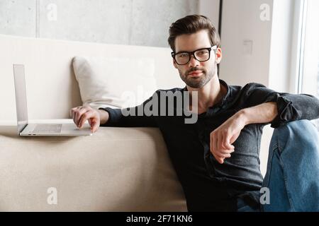 Focused unshaven man using laptop while sitting on floor at home Stock Photo