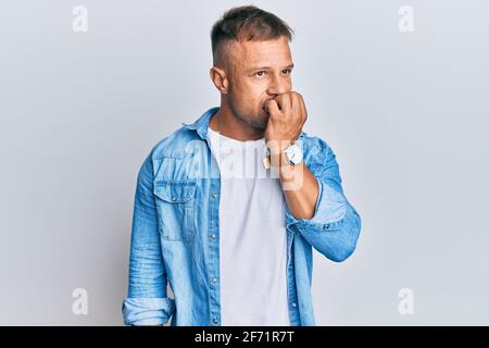 Handsome muscle man wearing casual denim jacket looking stressed and nervous with hands on mouth biting nails. anxiety problem. Stock Photo