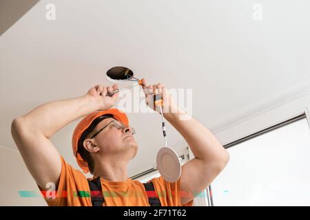 The electrician is installing an LED spotlight in the ceiling. Stock Photo