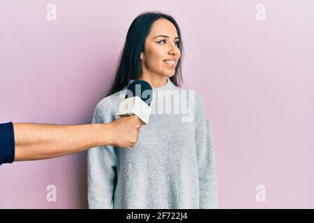 Young hispanic girl being interviewed by reporter holding microphone looking to side, relax profile pose with natural face and confident smile. Stock Photo