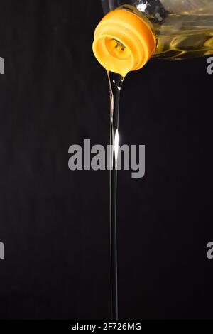 Pouring olive oil from a bottle on darck background. Stock Photo