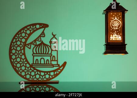 Eid Mubarak concepts with lamp inscribed with arabic text translated to english as Ramadhan is our light., with crescent moon in silhouette Stock Photo