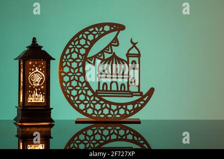 Eid Mubarak concepts with lamp inscribed with arabic text translated to english as Ramadhan is our light., with crescent moon in silhouette Stock Photo