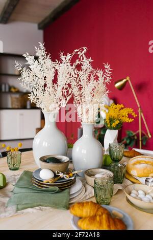Festive Easter table with eggs, pastries and fruit, two vases with dried flowers in the modern living room Stock Photo