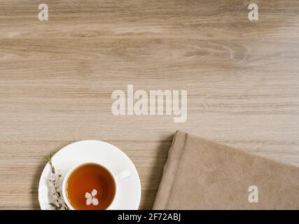 A white cup with black tea and a sprig of apple blossom and a photo album in a beige textile cover. Flat lay with copy space on wooden background Stock Photo