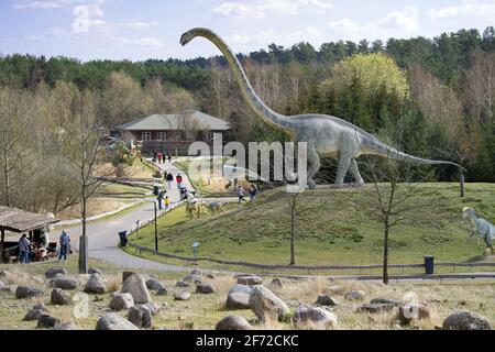 Brandeburg, Germany. 04th Apr, 2021. 04 April 2021, Brandenburg, Oranienburg/ Ot Germendorf: Visitors to the Animal, Leisure and Prehistoric Park walk past a Mamenchisaurus in sunny spring weather. Due to the relatively cool temperatures, there was little visitor rush at the park on Easter Sunday. Due to the Corona pandemic, official orders require visitors to comply with a number of requirements, such as handing over contact information upon entry, as well as wearing masks and keeping a minimum distance from strangers while visiting the zoo. Photo: Soeren Stache/dpa-Zentralbild/dpa Credit: dp Stock Photo