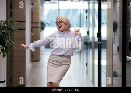 Excited middle-aged female employee dance in office Stock Photo