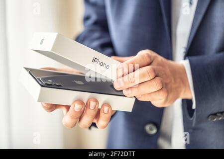Prague Czech Republic - 2. april 2021 - Businessman in suit holding in hands and opening a box with a brand new black apple iphone 12. Stock Photo