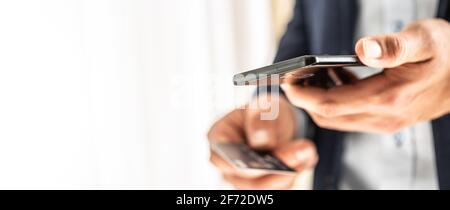 Handsome businessman in suit holding a smart phone in hand and paying by a credit card in local shop. Stock Photo