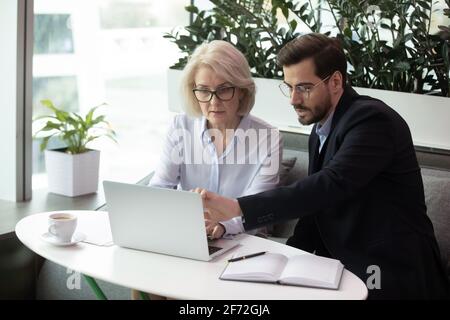 Diverse employees work on laptop in office together Stock Photo