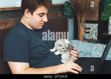 Young man with kitten working at his laptop. The concept of online learning and work during a pandemic. Stock Photo