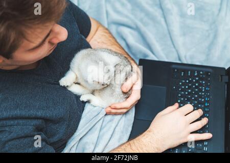 Young man with kitten working at his laptop. The concept of online learning and work during a pandemic. Stock Photo