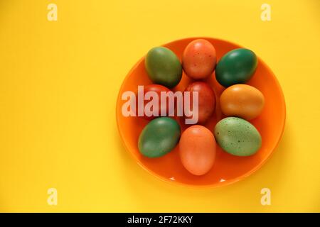 Colorful painted traditional easter eggs on orange plate, beautiful decoration on yellow background copy space Stock Photo