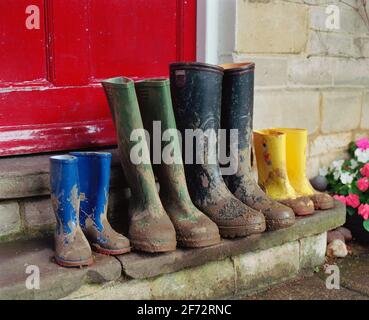 A family of wellington boots left on a doorstep with a red door behind. Stock Photo