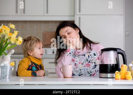 Tired mother, trying to pour coffee in the morning. Woman lying on kitchen table after sleepless night, trying to drink coffee Stock Photo