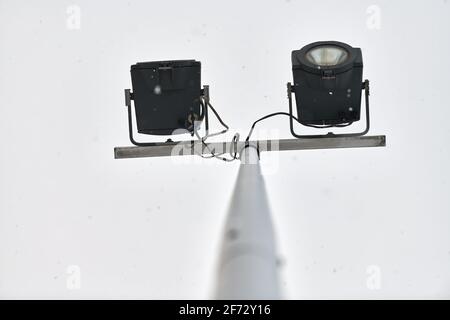 Powerful LED light on aluminum metal pole, cloudy grey sky background with snowflakes. LED street light, car park lamp. Modern light source. Stock Photo