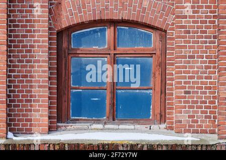 One arched glass window on old red brick wall. Vintage window in brown wooden frame on red brick wall of industrial building. Stock Photo
