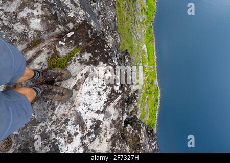 Hiker standing on steep cliff, vertical drop to fjord, Mount Barden, Senja, Norway Stock Photo