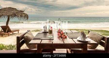 Romantic dinner in beach restaurant or cafe, Sri Lanka. Table with cocktail and flowers on ocean background in tropical resort, beautiful panoramic vi Stock Photo