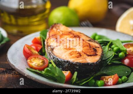 Roasted salmon steak with spinach and tomato salad on a plate, closeup view Stock Photo