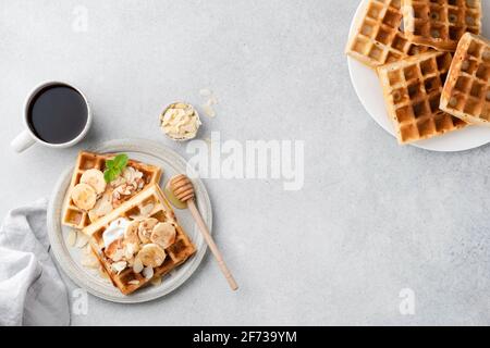 Banana Caramel Belgian Waffles On Plate Served With Almonds, Cream And Cup Of Coffee. Top View. Sweet Breakfast Food With Copy Space Stock Photo