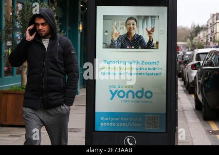 London, UK. 03rd Apr, 2021. A man speaking on the mobile phone walks past an advert by Yondo about 'Tutoring with Zoom?' in London. Credit: SOPA Images Limited/Alamy Live News