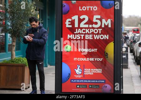 London, UK. 03rd Apr, 2021. A man stands next to 'Lotto £12.5m Jackpot must be won' advertisement in London. Credit: SOPA Images Limited/Alamy Live News