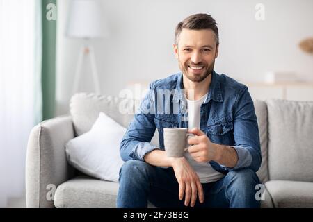 Positive handsome man drinking coffee in living room Stock Photo