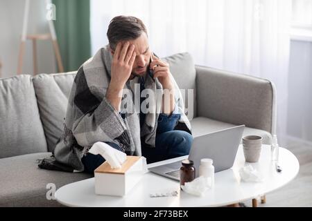 Sick man working on laptop at home, talking on phone Stock Photo