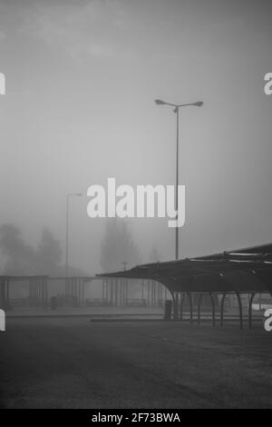 A vertical dark misty scene with a view of a morning empty parking on the territory of a gas filling station with a curved metal roof of a shed agains Stock Photo