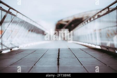 View of a long bright overhead passage or a pedestrian bridge stretching into the distance, glass walls and chrome banister, shallow depth of field wi Stock Photo