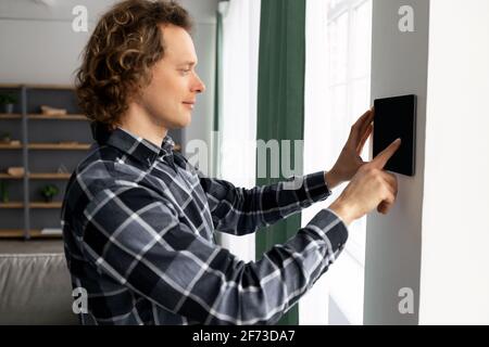 Guy Using Tablet On Wall With Smart Home Application Indoors Stock Photo