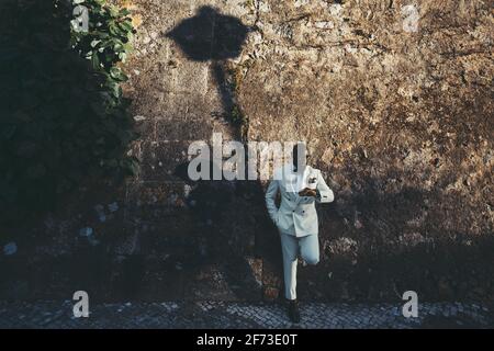 A dapper bald bearded black guy in a fashionable white costume and eyeglasses is waiting for his girlfriend to have dinner together, looking at his wa Stock Photo