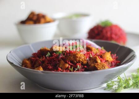 Beetroot pulao, a one pot rice preparation with basmati rice, beetroot, onions and spices. Served with air fried chicken bites and curd. Shot on white Stock Photo