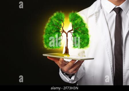 Doctor holding tablet computer with drawing of green tree in shape of human lungs on dark background Stock Photo