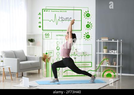 Virtual screen of heart rate monitor and sporty young woman practicing yoga at home Stock Photo