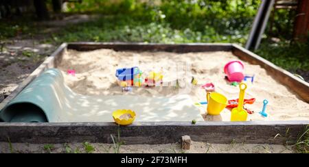 Sandbox outdoor. Children's wooden sandbox with various toys for the game. Summer concept. Selective focus with shallow depth of field Stock Photo