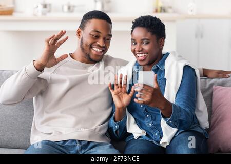 Black couple having videocall using smartphone waving hands Stock Photo