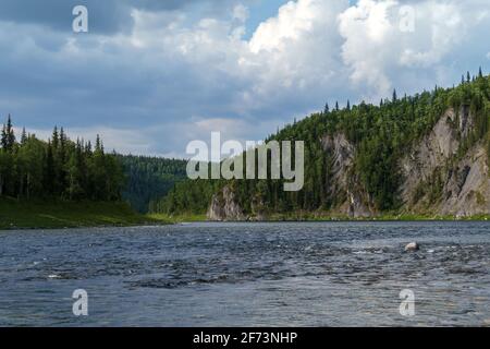 View from the river to the rocky shore. Cliffs overgrown with forest. The landscape of the Northern nature Stock Photo