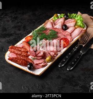 Assorted meat products, including ham, sausage, balyk, lard, basturma, prosciutto on dark background Stock Photo