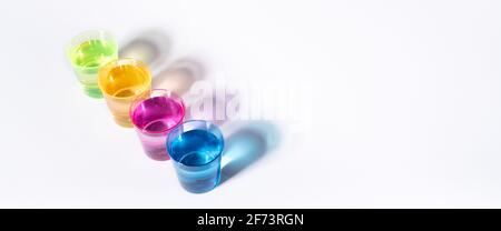 Plastic multi-colored glasses with liquid on a white background with highlights. Layout, mockup. Stock Photo
